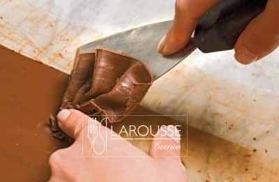 <p>Raspar el chocolate siguiendo una línea recta y sujetando con una mano una espátula triangular de metal en un ángulo de 45º; detener por una de las orillas el chocolate que se vaya desprendiendo con el dedo índice de la mano contraria. Repetir esta operación para obtener más holanes o abanicos.</p>
