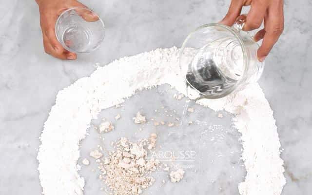 <p>Forme con la harina un círculo sobre una superficie plana y añada en el centro la levadura y el agua. Disuelva la levadura en el agua e incorpórela paulatinamente a la harina.</p>
