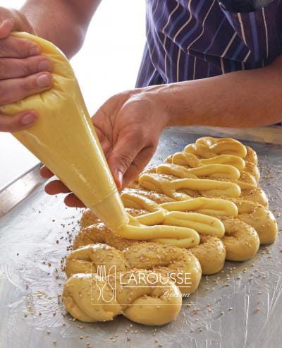 <p>Bata la crema pastelera con un batidor globo e introdúzcala en la manga con duya. Espolvoree la superficie de la masa con el ajonjolí y decórela con la crema siguiendo la misma forma de la trenza o el mismo movimiento de zigzag.</p>

